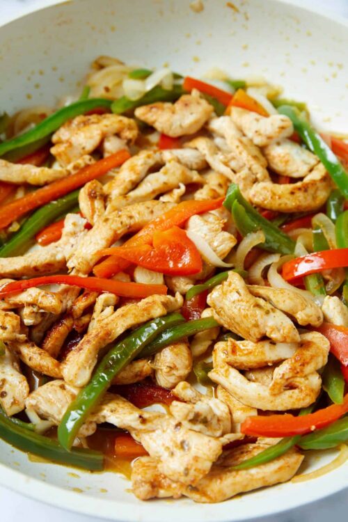 Sautéed chicken with colorful bell peppers in a white serving dish.