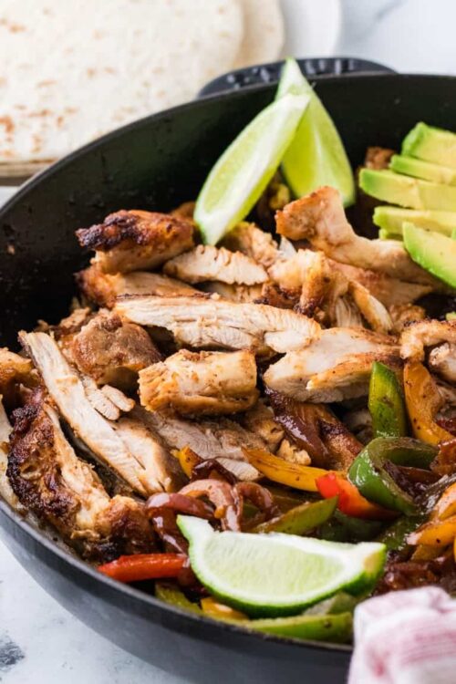 Grilled chicken with fresh lime and colorful sautéed bell peppers served in a black skillet.