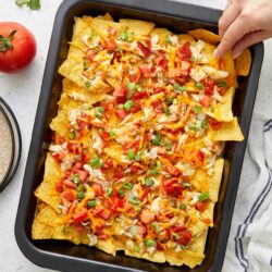 Crab nachos with cheese, tomatoes, and green onions on a baking sheet.