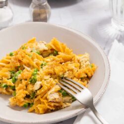 Creamy chicken pot pie filling with peas in a white bowl on marble surface.