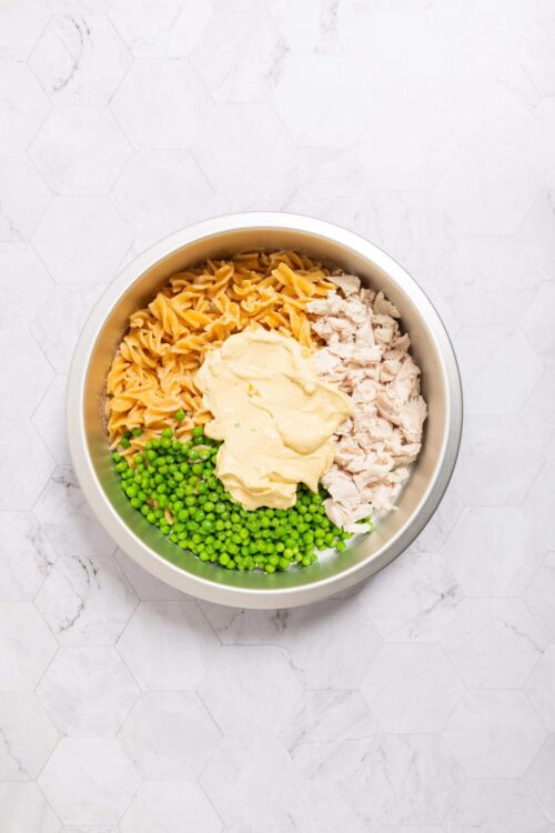 Cream cheese chicken casserole ingredients in a mixing bowl with shredded chicken, peas, fettuccine, and cream cheese.