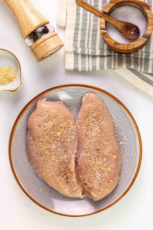 Marinated chicken breasts with herbs and spices on a ceramic plate.