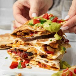 Crispy chicken quesadilla with guacamole and fresh tomato toppings on white surface.