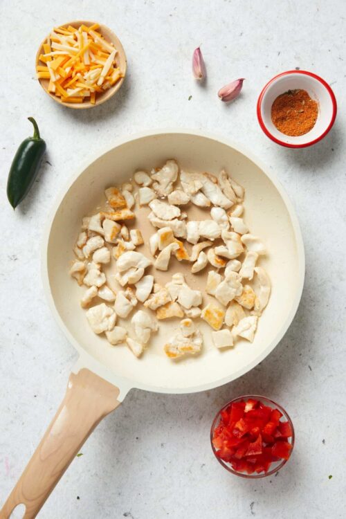 Creamed chicken cooking in a cast iron skillet with chopped vegetables on the side.