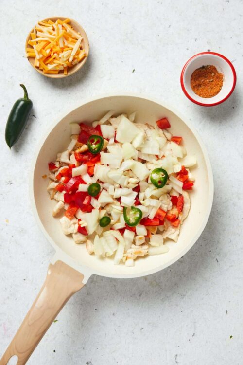 Shredded cheese, chopped vegetables, and chicken in a white pot ready for baking or cooking.