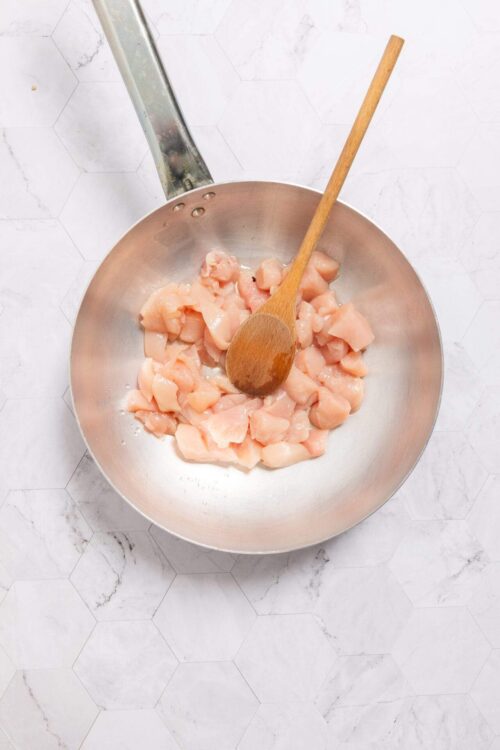 Raw chicken cubes in a stainless steel skillet.