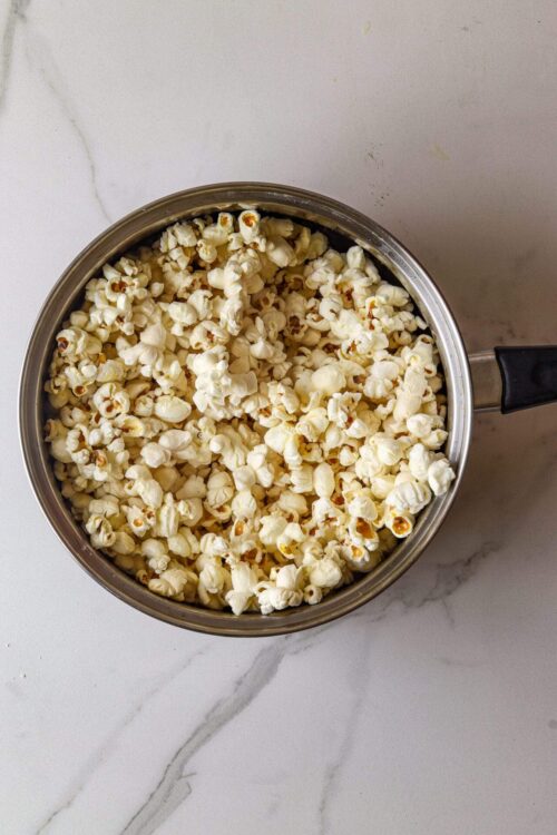 Buttery popcorn in a stainless steel pot on white marble surface, perfect for movie night or snacking.