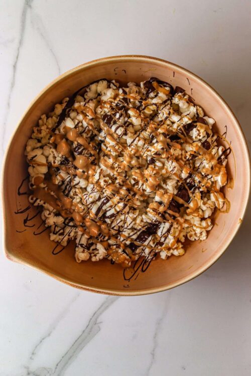 Buttered popcorn with chocolate and caramel drizzle in a beige bowl on marble surface.