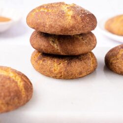 Buttery snickerdoodle cookies stacked on a white surface with a light background.