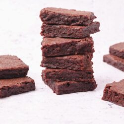 Rich chocolate brownies stacked on a white background.
