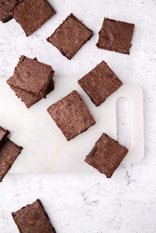 Fudgy chocolate brownie squares on white cutting board, baked dessert, homemade treat.