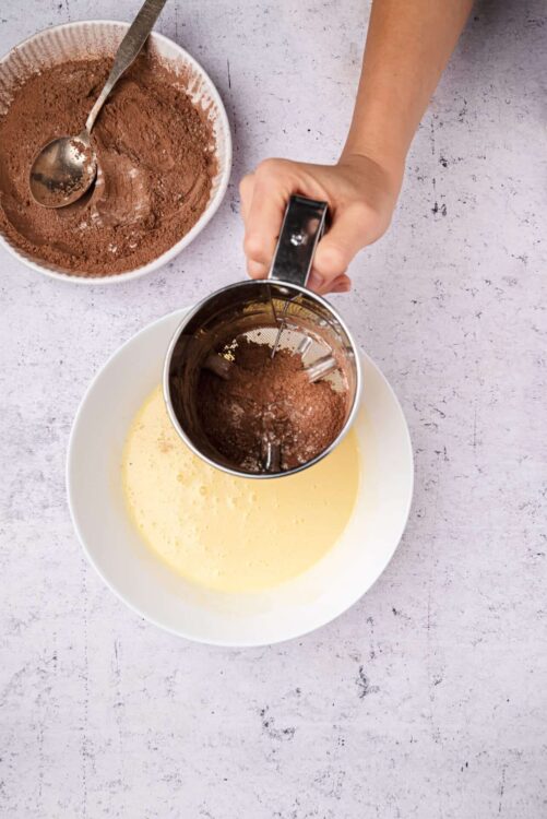 Filling a sifter with cocoa powder over a bowl of creamed butter and sugar for baking.