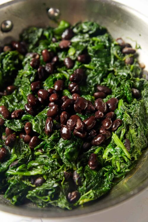 Sautéed spinach with black beans in a skillet, healthy vegetarian vegetable dish.