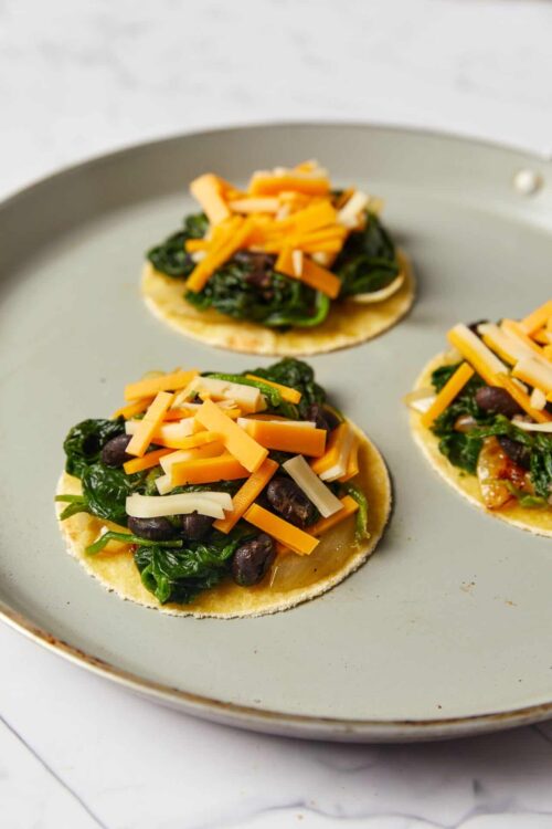 Mini vegan black bean and spinach tacos on corn tortillas, topped with shredded cheese. Perfect for quick, healthy plant-based meals.