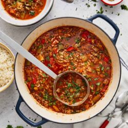 Hearty vegetable lentil soup in a large pot with fresh herbs and rice on the side.