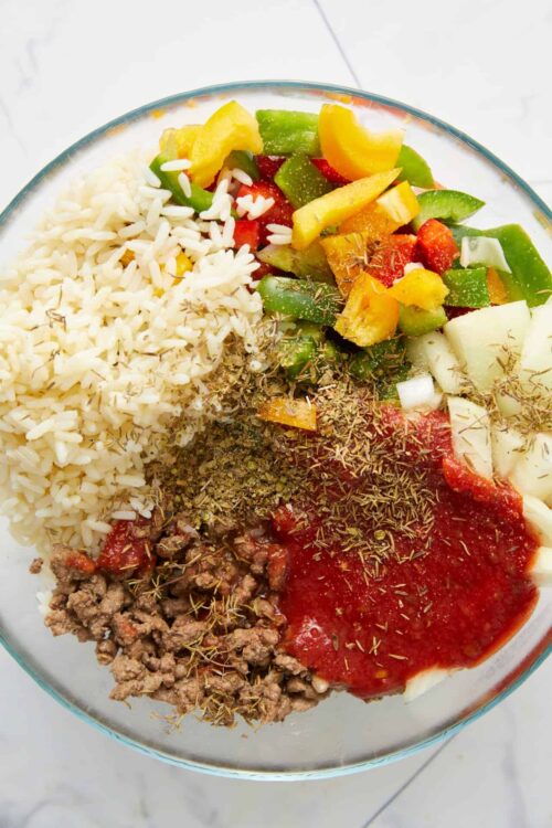 Fresh Mexican taco ingredients with seasoned ground beef, rice, chopped vegetables, and herbs in a clear glass bowl.