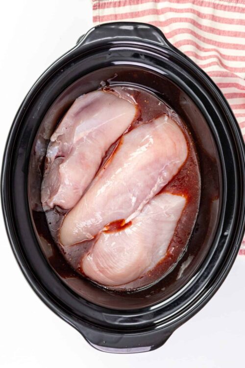 Seasoned raw chicken breasts in a slow cooker with marinade.