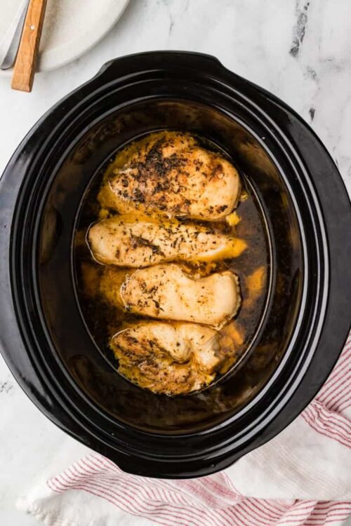 Baked chicken breasts cooking in a slow cooker with herbs and spices.