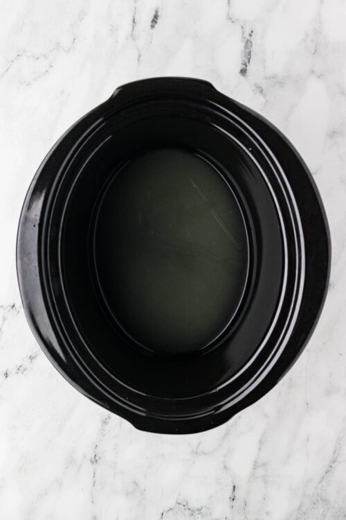 Non-stick slow cooker insert with empty interior, black oval crockpot for cooking.