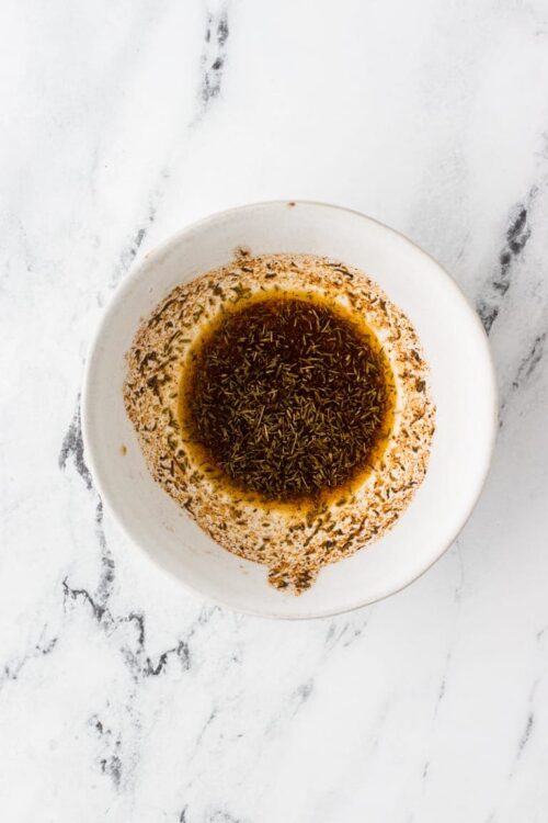 Sun-dried tomato and herb marinade in a white bowl on marble surface.