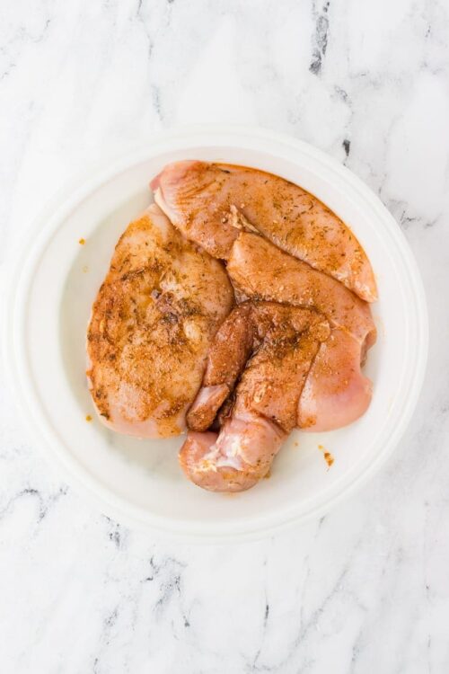 Raw chicken thighs seasoned with spices for baking or frying.