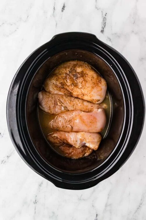 Boneless chicken breasts with seasoning in a slow cooker, ready for cooking or recipe preparation.