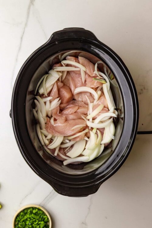 Sliced chicken and onions in a slow cooker for homemade chicken recipe.