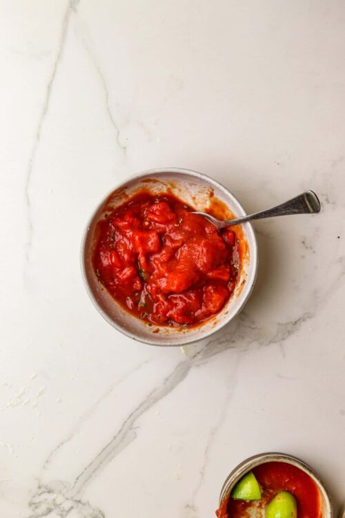 Savory tomato basil sauce in a white bowl with a spoon on marble surface.