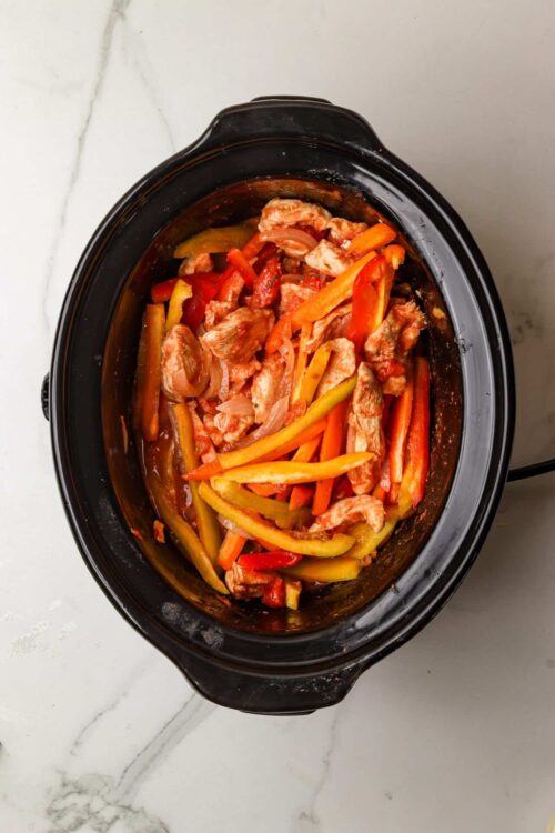 Sliced chicken and colorful bell peppers cooking in a slow cooker for a healthy savory meal.