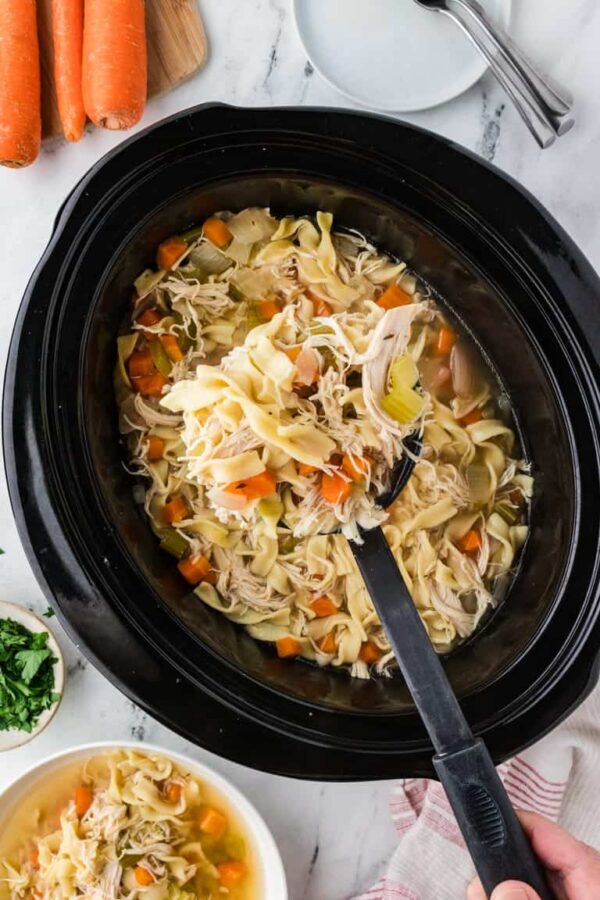 Comforting homemade chicken and noodle soup in a slow cooker with tender shredded chicken and fresh vegetables.