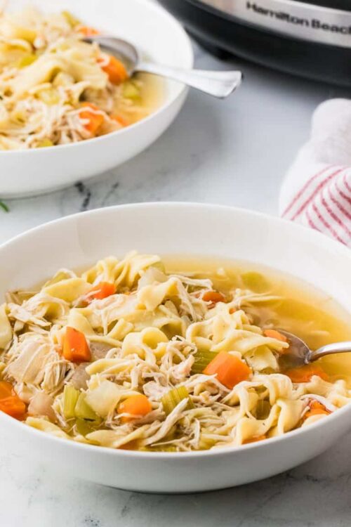 Comforting chicken noodle soup with vegetables in white bowls, perfect for cold days.