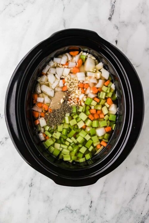 Chopped vegetables and seasonings in slow cooker for soup or stew preparation.