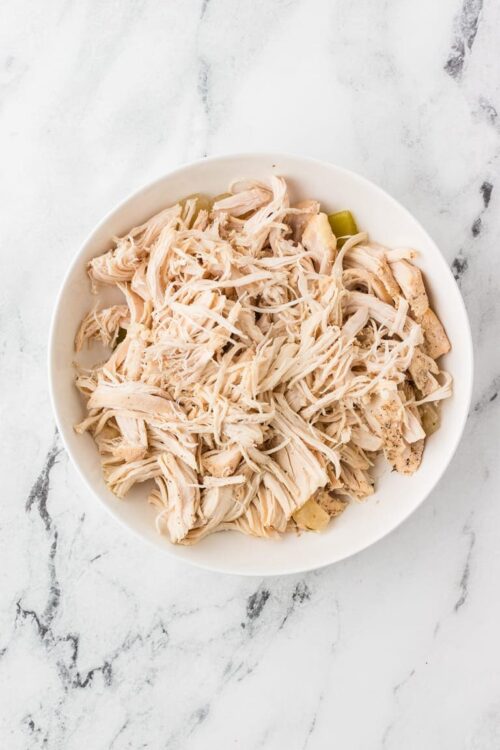Shredded cooked chicken in white bowl on marble surface.