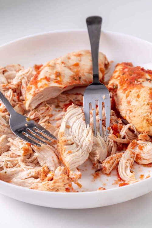 Succulent shredded chicken in a white baking dish with fork and spatula, perfect for easy homemade chicken recipes.