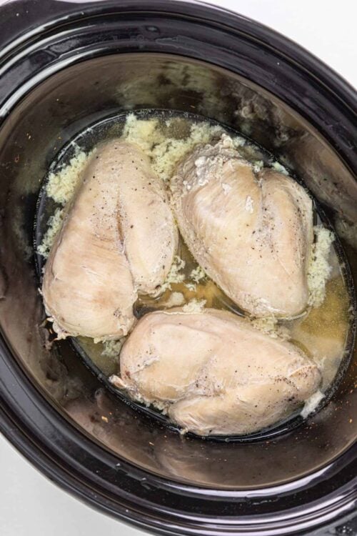 Poached chicken breasts in a slow cooker with garlic and herbs.