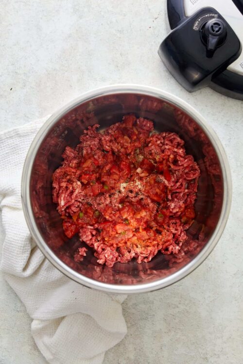 Minced beef with chopped tomatoes and spices in a slow cooker, ready for cooking.