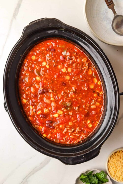 Rich slow cooker chili with beans and ground beef in a black crockpot.