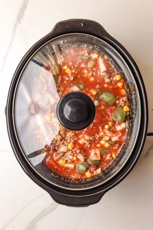 Stew in a slow cooker with ground beef, vegetables, and tomato sauce.