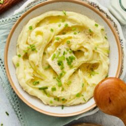 Creamy mashed potatoes with chopped chives and black pepper on a white plate.
