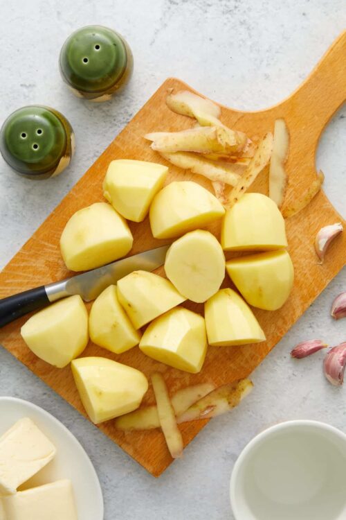 Golden boiled potatoes on a wooden cutting board with garlic and seasoning.