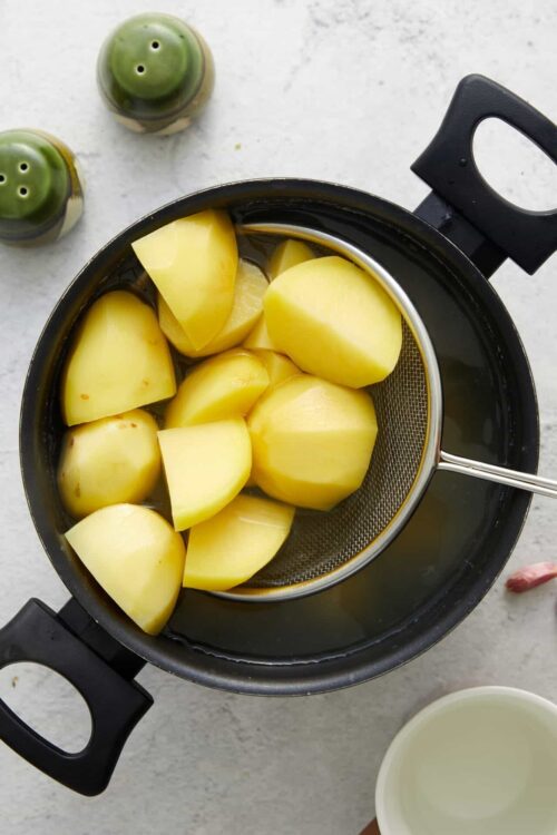 Soft boiled potatoes in a black pot with a metal strainer.