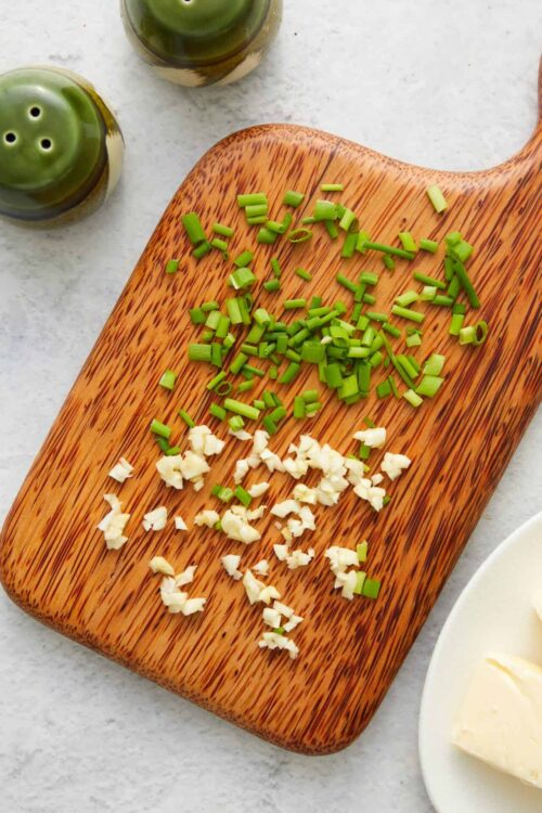 Chopped green onions and garlic on a wooden cutting board for cooking or garnishing.