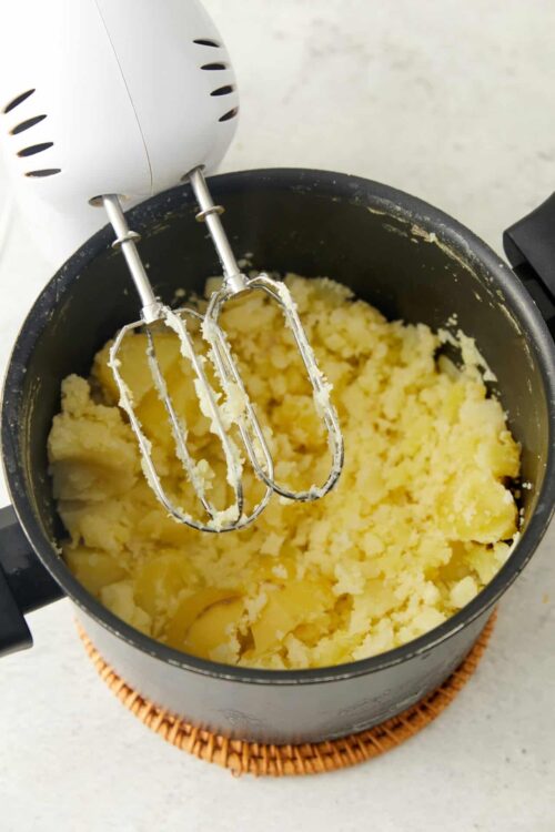Creamy mashed potatoes in a black pot with hand mixer beaters.
