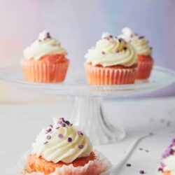 Cream cheese frosting cupcakes with purple sprinkles on white background.