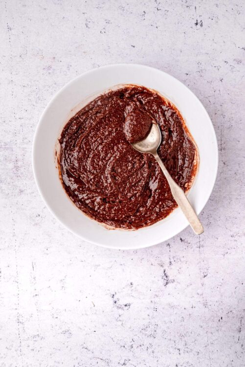 Rich homemade chocolate fudge sauce in a white bowl with spoon.
