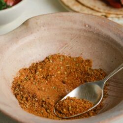 Ground spice blend in a pink ceramic bowl with a silver spoon.