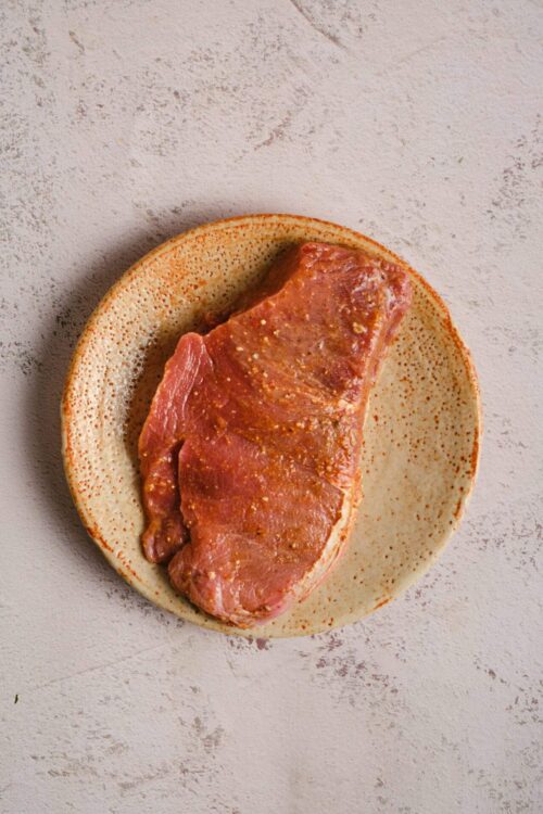 Raw seasoned pork chop on a rustic ceramic plate for grilling or baking.