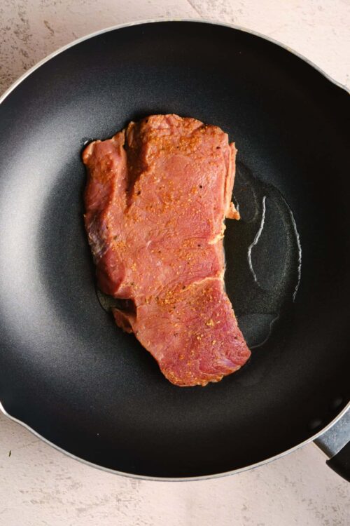 Juicy seasoned flank steak cooking in a non-stick skillet for flavorful beef dishes.