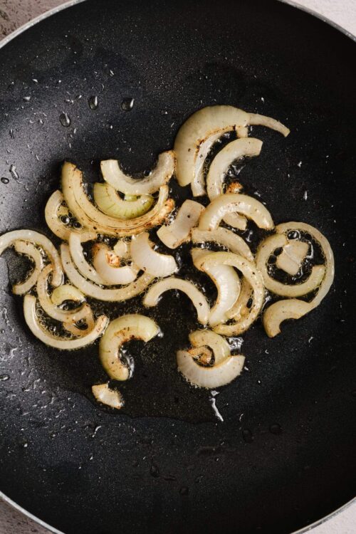 Sautéed onions cooking in a black skillet for caramelization or flavor enhancement.
