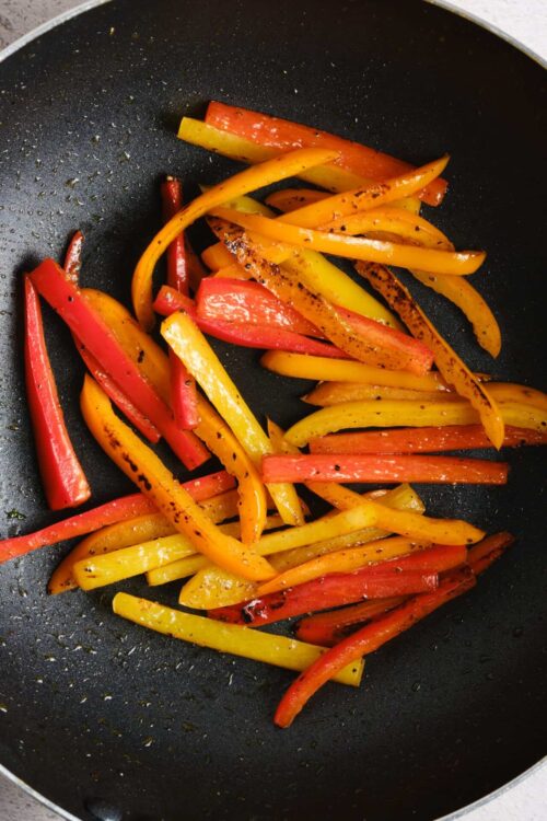 Colorful sautéed bell peppers in a black skillet, seasoned and lightly charred, perfect for healthy recipes or side dishes.